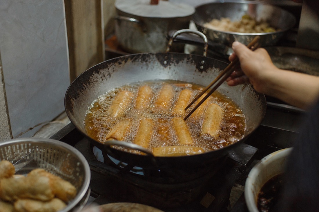Golden spring rolls frying in a wok of oil in a Hanoi home kitchen with steam rising