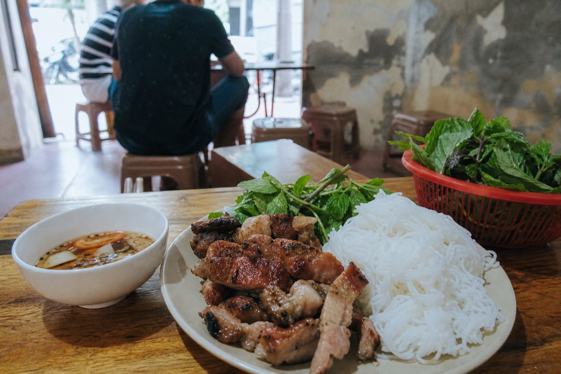 Home-cooked plate of barbecued pork, rice vermicelli and dipping sauce arranged on a wooden table in Hanoi in natural daylight