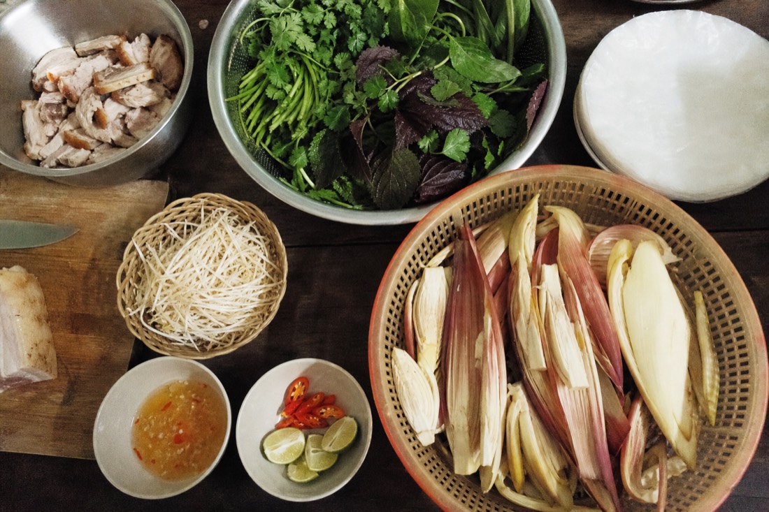 Fresh market ingredients, banana flower, herbs, pork and rice paper laid out ready on a kitchen bench in Hanoi, overhead angle