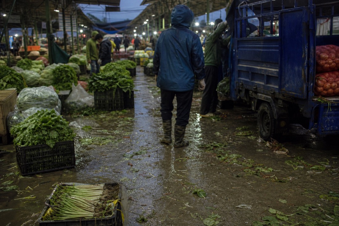 Wet concrete market floor with fallen leaves and produce crates at a busy Hanoi wholesale market before sunrise
