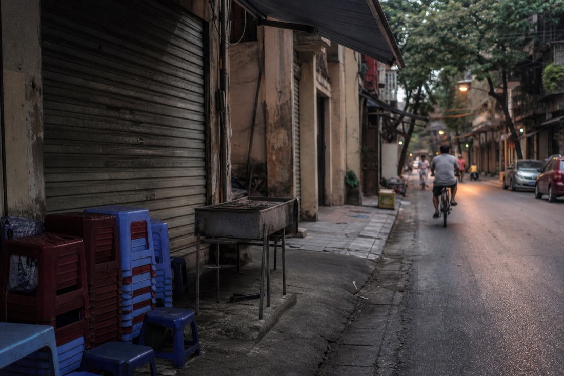 Shuttered bun cha shopfront with stacked stools and a cold grill on a quiet Old Quarter street in early evening light in Hanoi