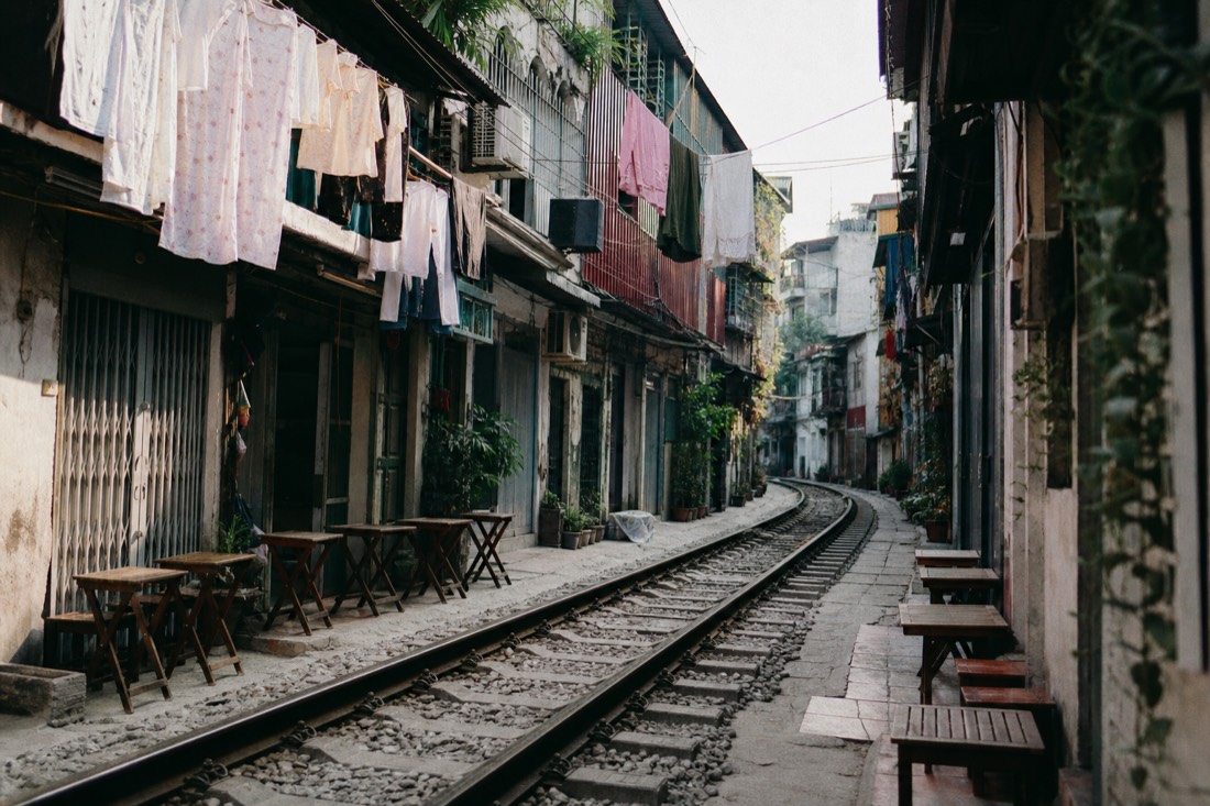 Empty Train Street corridor with laundry hanging above the tracks and closed cafe stools in soft late-afternoon light in Hanoi