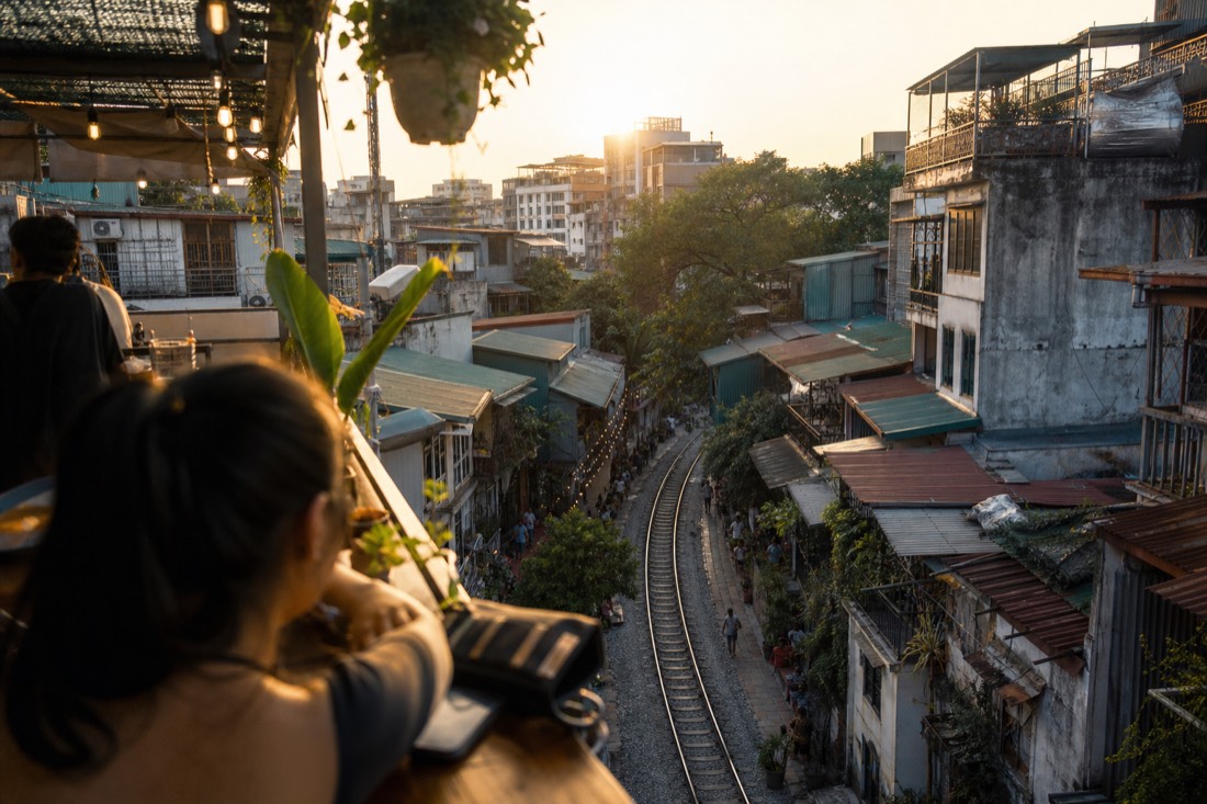 View from a second-floor cafe balcony over the Train Street tracks and rooftops at golden hour in Hanoi