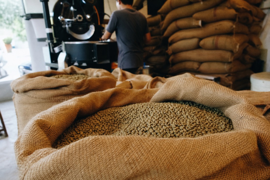 Raw robusta coffee beans and burlap sacks stacked at a small roasting operation in Vietnam under warm interior light