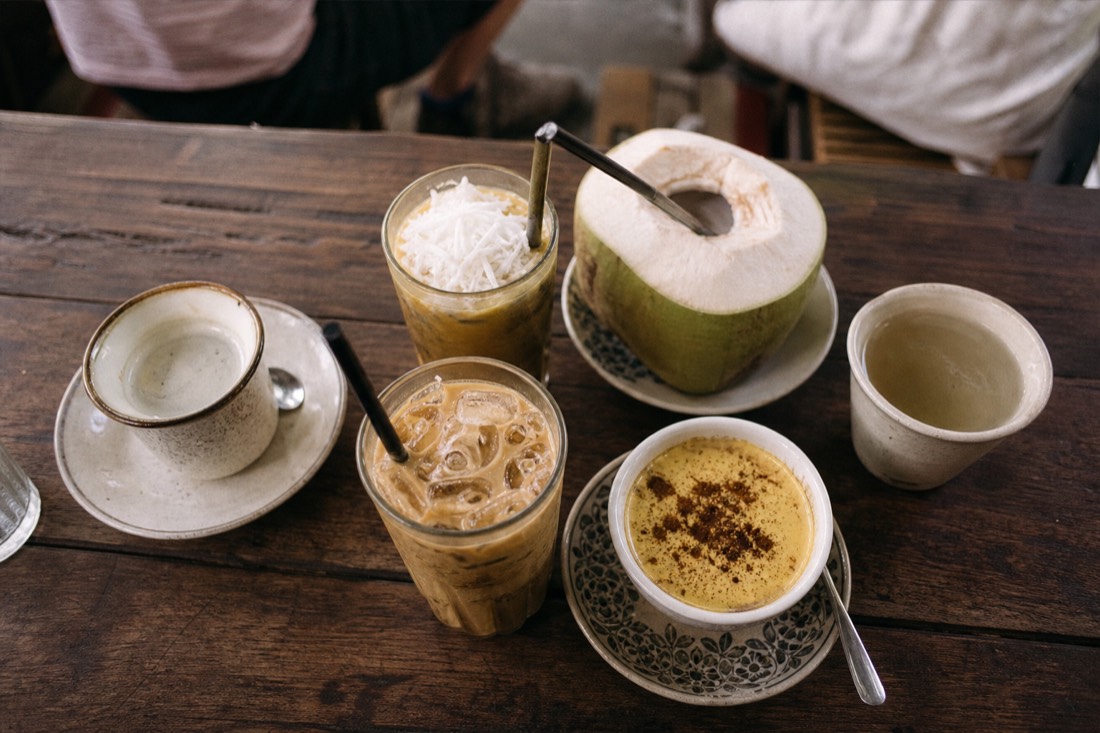 Several different Vietnamese coffee drinks, egg coffee, coconut coffee and iced milk coffee, arranged together on a wooden cafe table from overhead