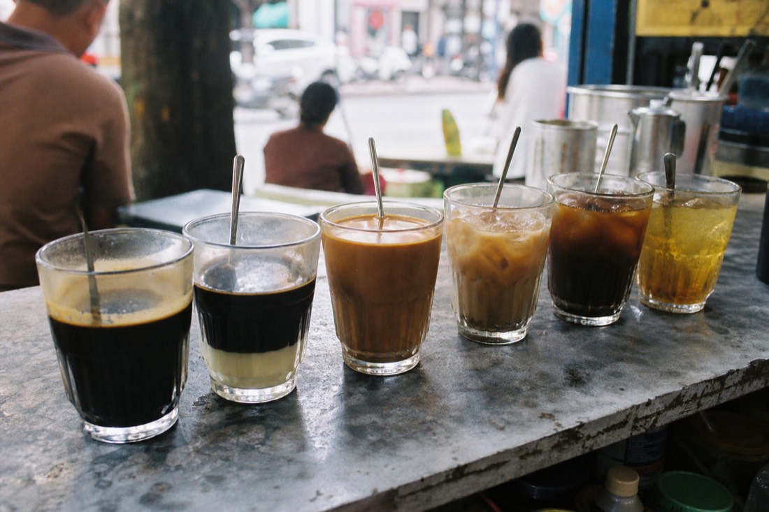 Row of small tasting glasses holding different Vietnamese coffee styles lined up on a cafe counter in natural light