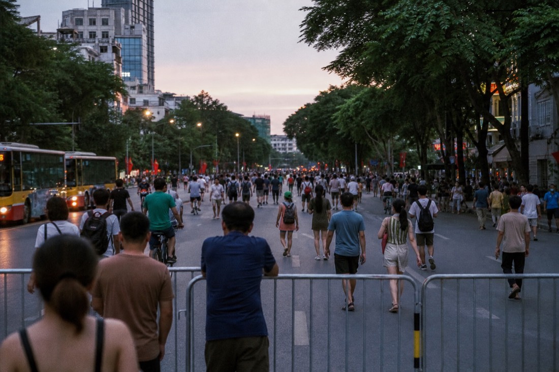 Pedestrian barrier across a Hanoi street at dusk with crowds beginning to walk in the space where traffic used to run