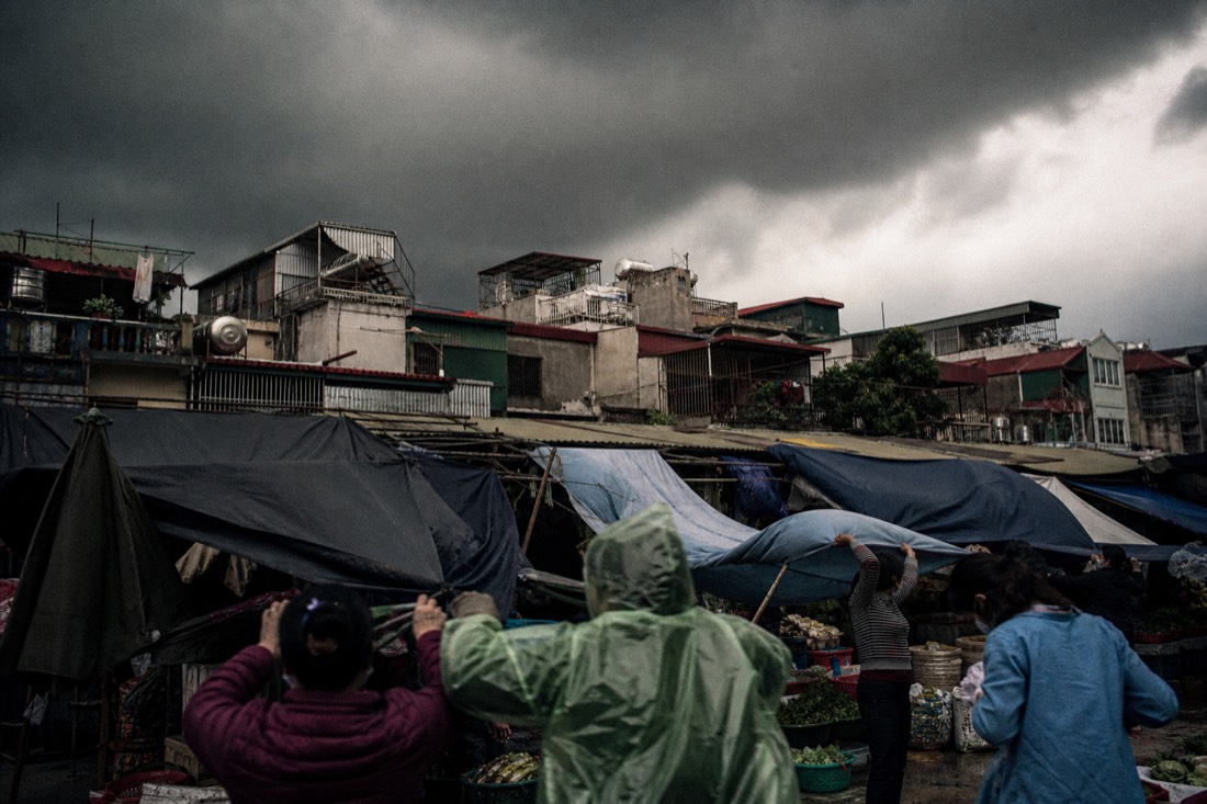 Dark storm clouds gathering over Hanoi rooftops as vendors pull tarps over stalls