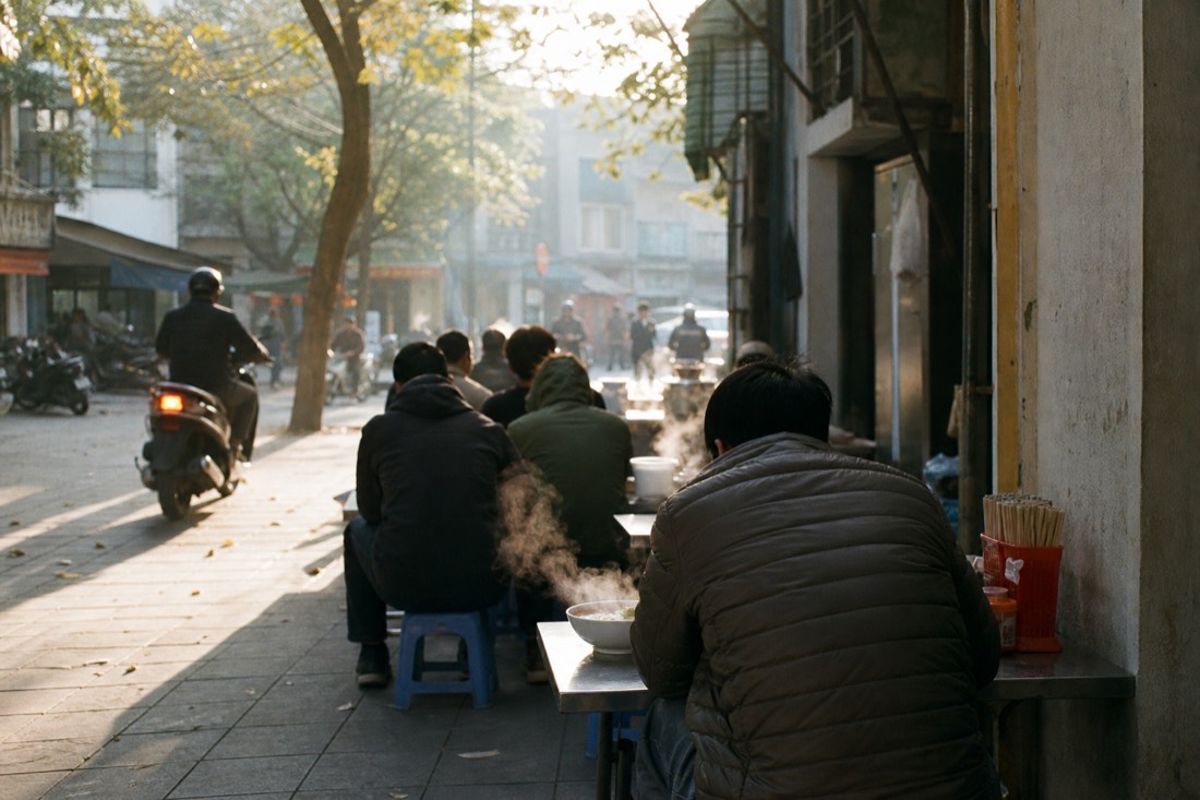 Cool November morning on a Hanoi street with people in light jackets eating pho at pavement tables