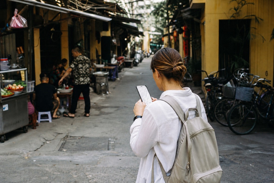 Solo traveller checking a phone map at a quiet Hanoi street corner near food stalls in daylight