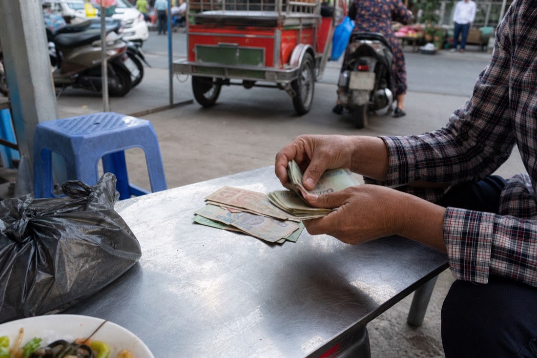 Hand counting out Vietnamese dong banknotes on a low steel table at a street food stall