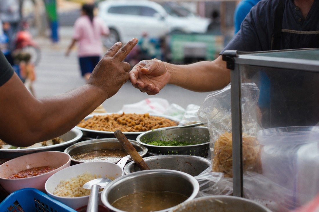 Vendor and customer communicating with hand gestures over a street food cart, ordering by counting fingers