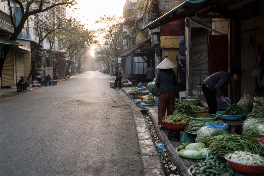 Vendors setting up baskets of produce at a Hanoi market at dawn with empty streets