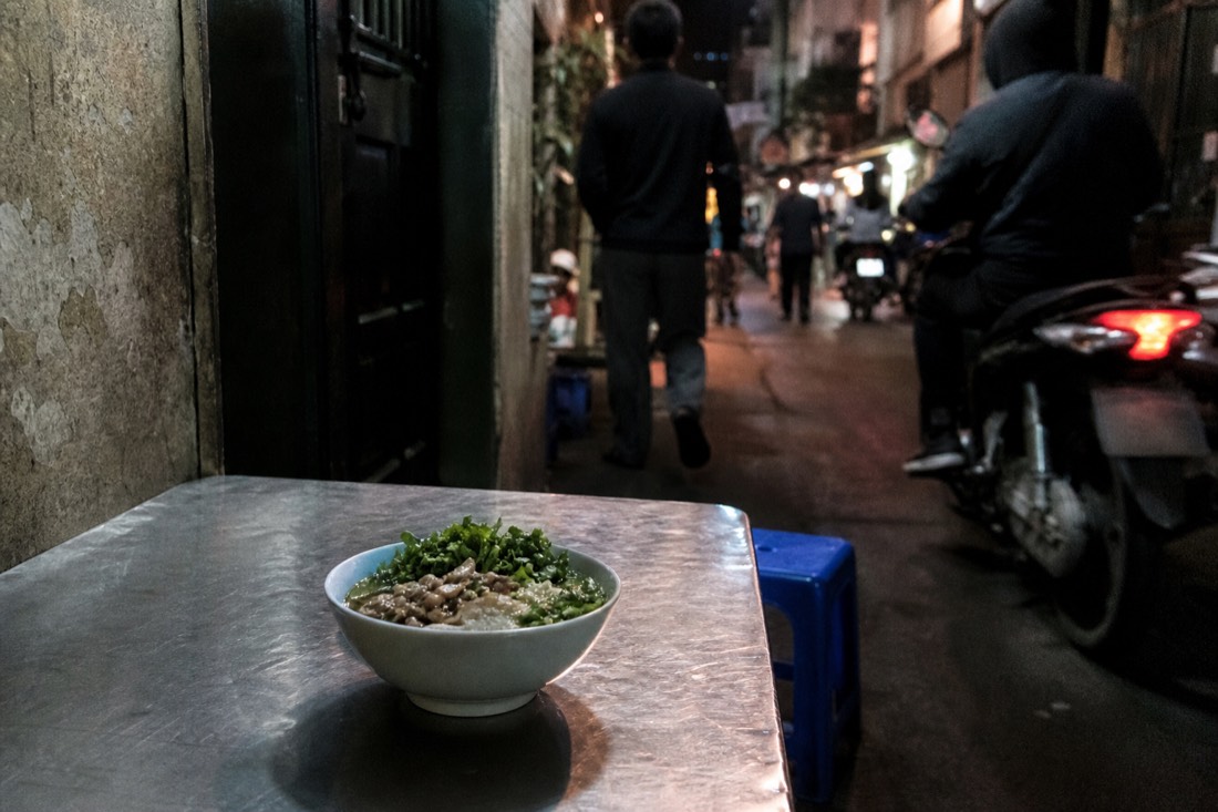 Traveller eating a bowl of noodles at a self-guided street food stop in a narrow Hanoi Old Quarter lane