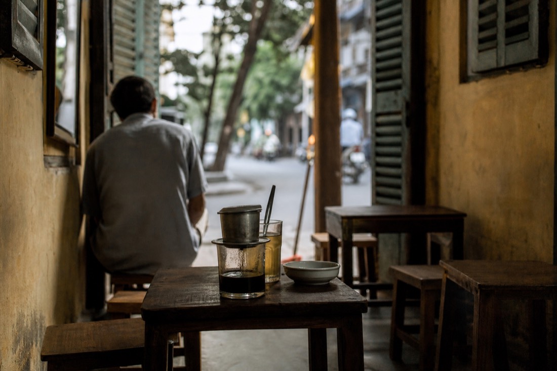 Vintage-style narrow Hanoi cafe interior with a phin coffee filter dripping into a cup in morning light