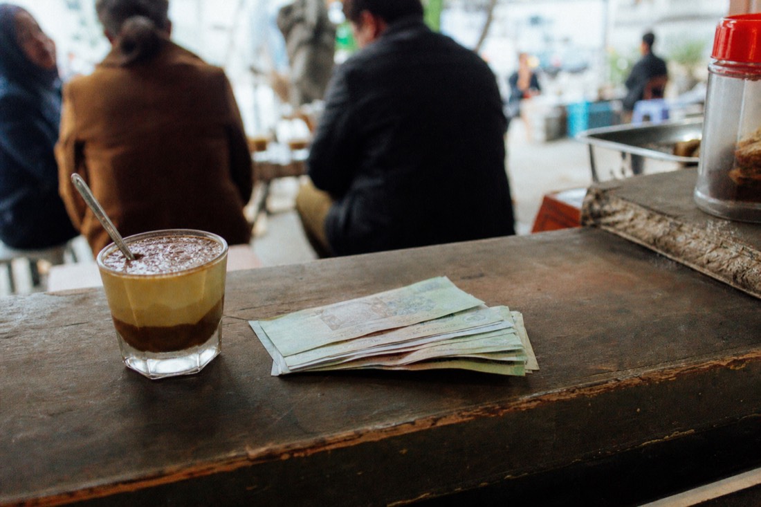 Small stack of Vietnamese dong banknotes beside an egg coffee cup on a cafe counter