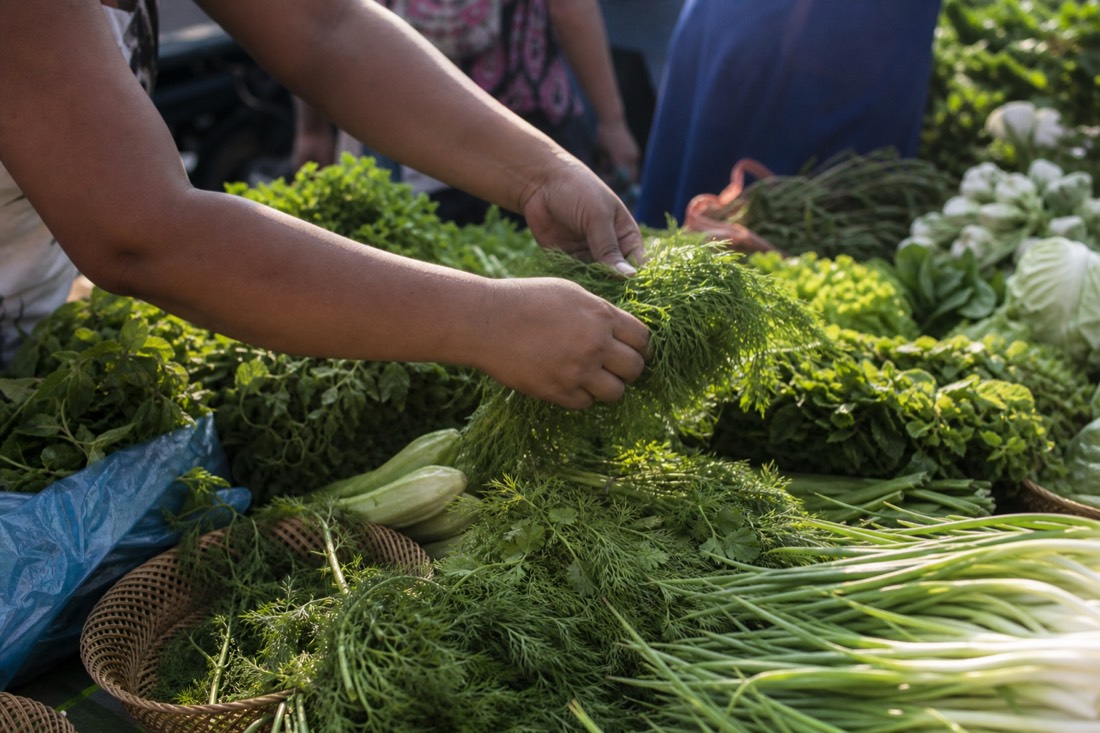 Hands selecting fresh herbs and vegetables at a Hanoi market stall for a cooking class