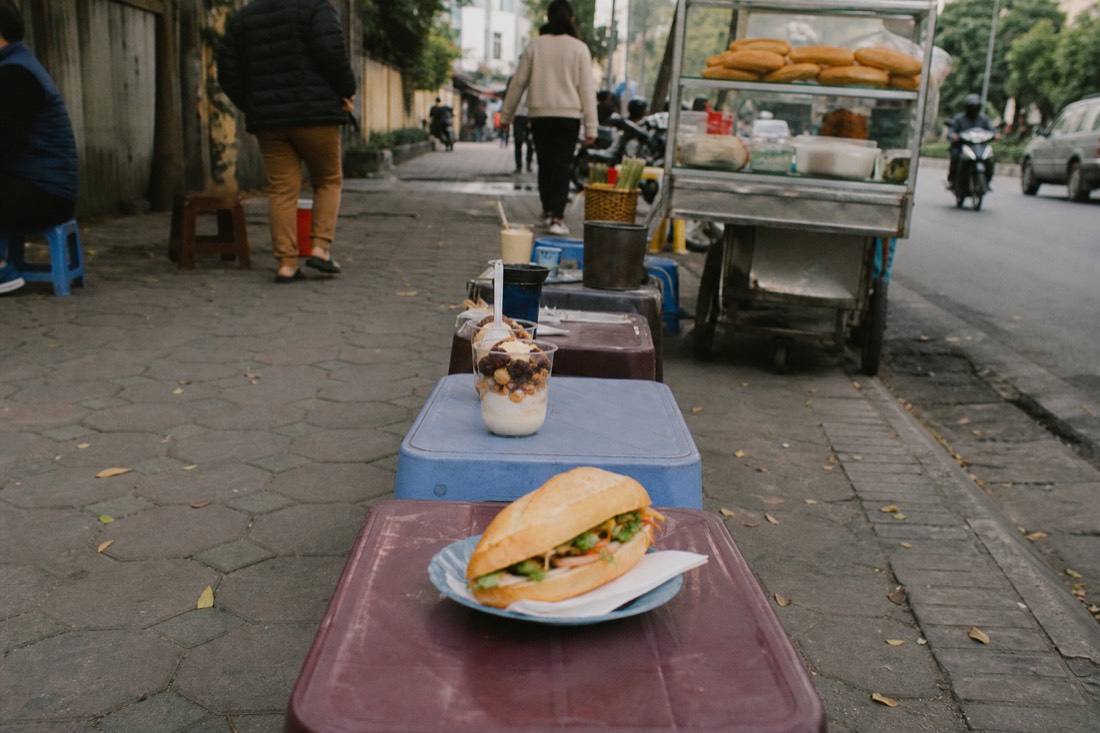Row of small street food stops with different snacks laid out along a Hanoi pavement