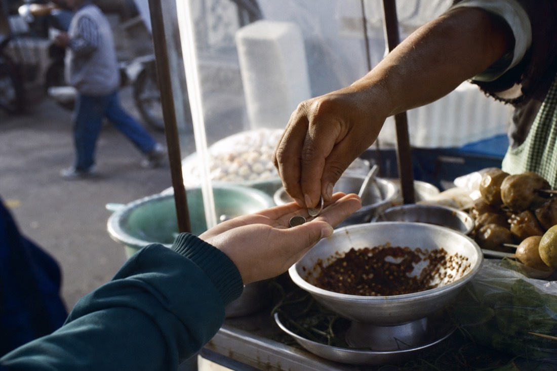 Street vendor handing change to a customer over a food cart at a Hanoi stall