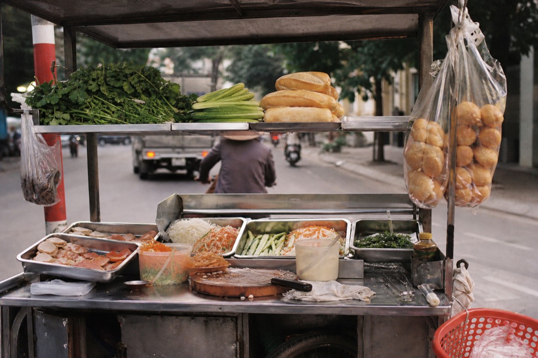 Vendor's stainless steel cart stocked with fresh ingredients for banh mi assembly