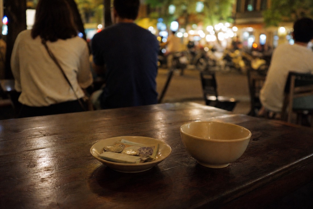 Small saucer with loose coins and folded small notes left beside an empty bowl on a restaurant table