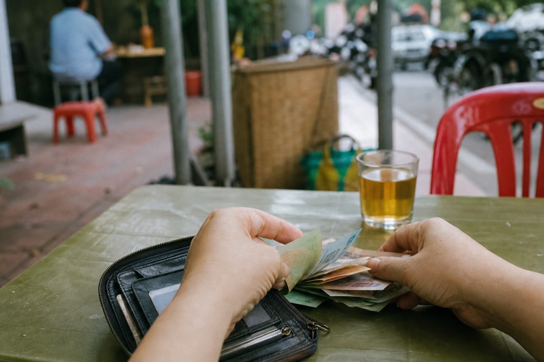Open wallet on a cafe table showing small Vietnamese banknotes being sorted by hand