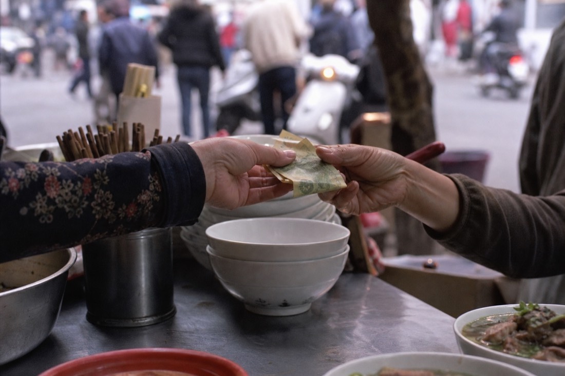 Small Vietnamese dong banknotes being handed across a Hanoi street food counter
