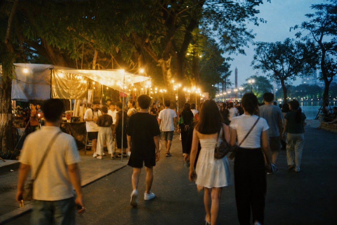 Crowd of pedestrians walking a car-free street lined with food stalls near Hoan Kiem Lake at night