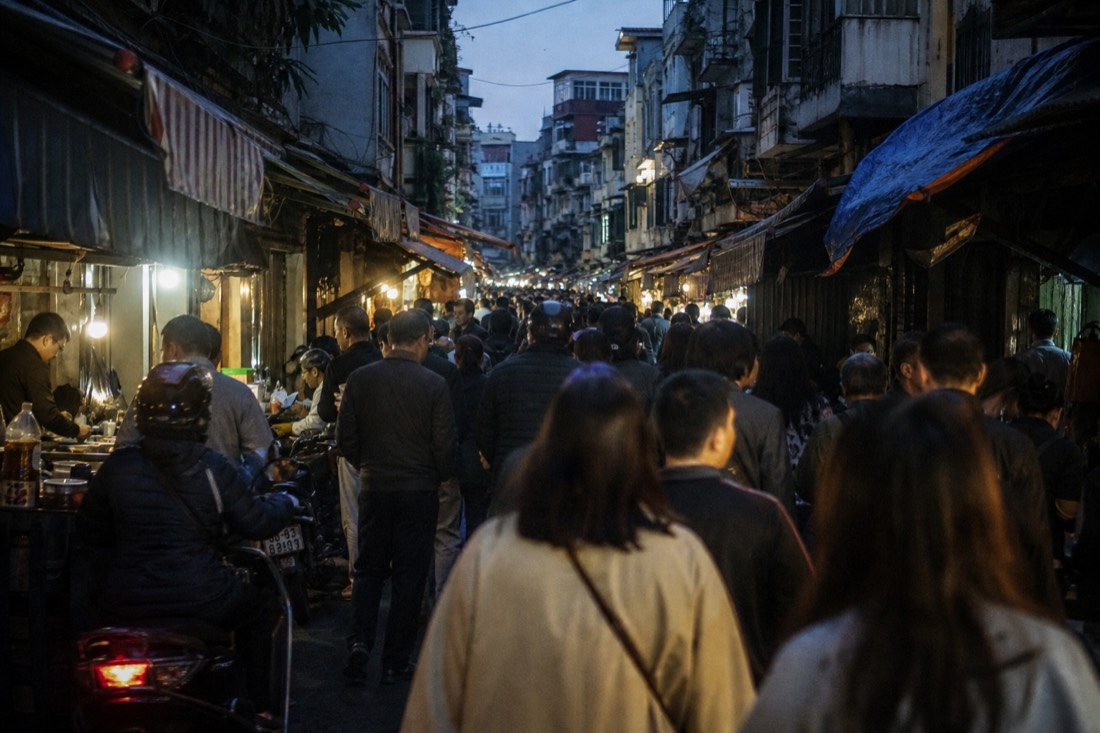 Dense evening foot traffic squeezing through a narrow Old Quarter lane in Hanoi