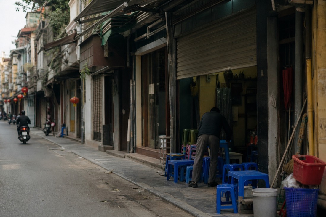 Empty Old Quarter street with a single food stall's shutters half-raised in the quiet hour between lunch and dinner