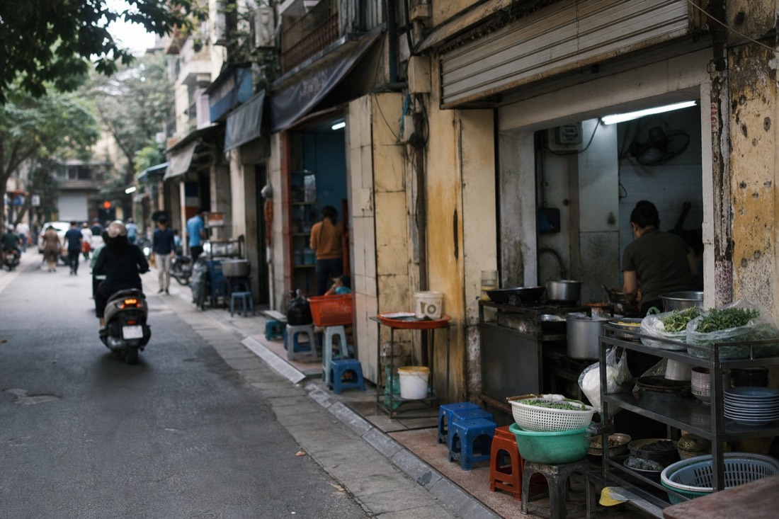 Row of narrow shopfronts each specializing in a different dish along a Hanoi food street