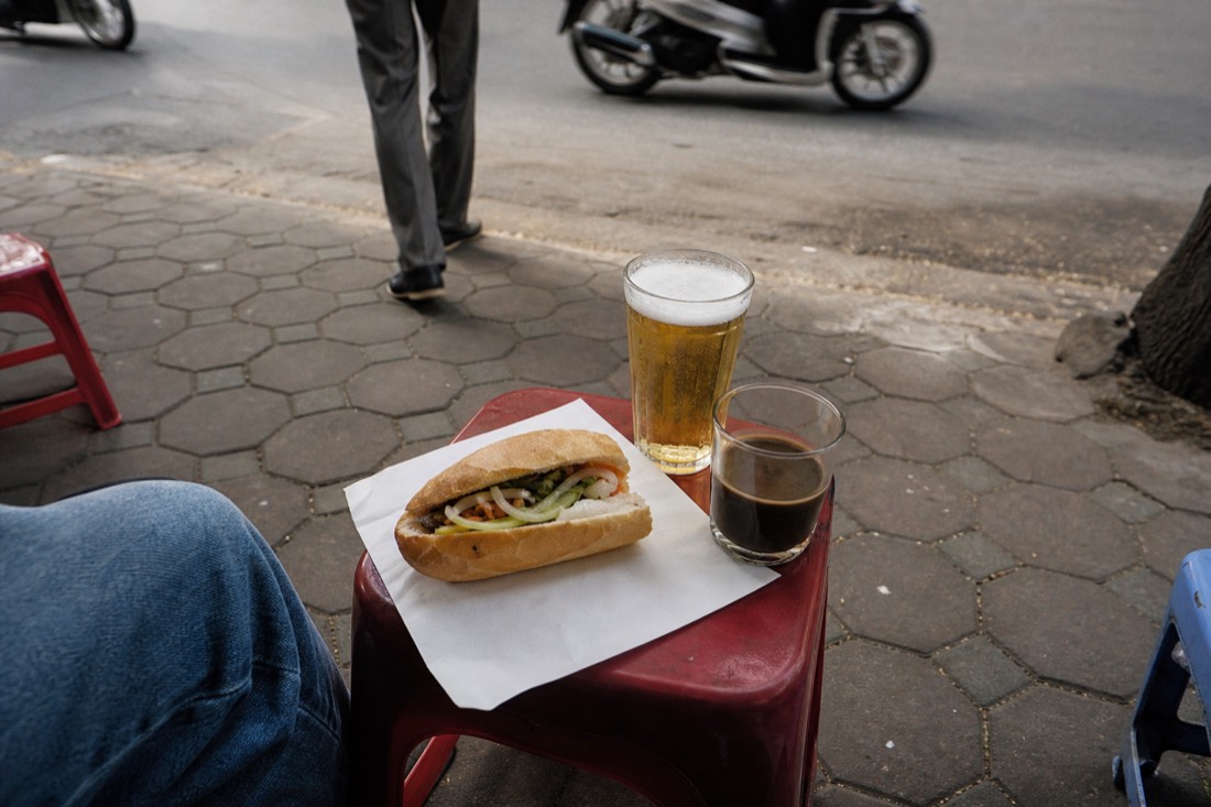 Assortment of Hanoi street snacks and a glass of bia hoi arranged on a low stool