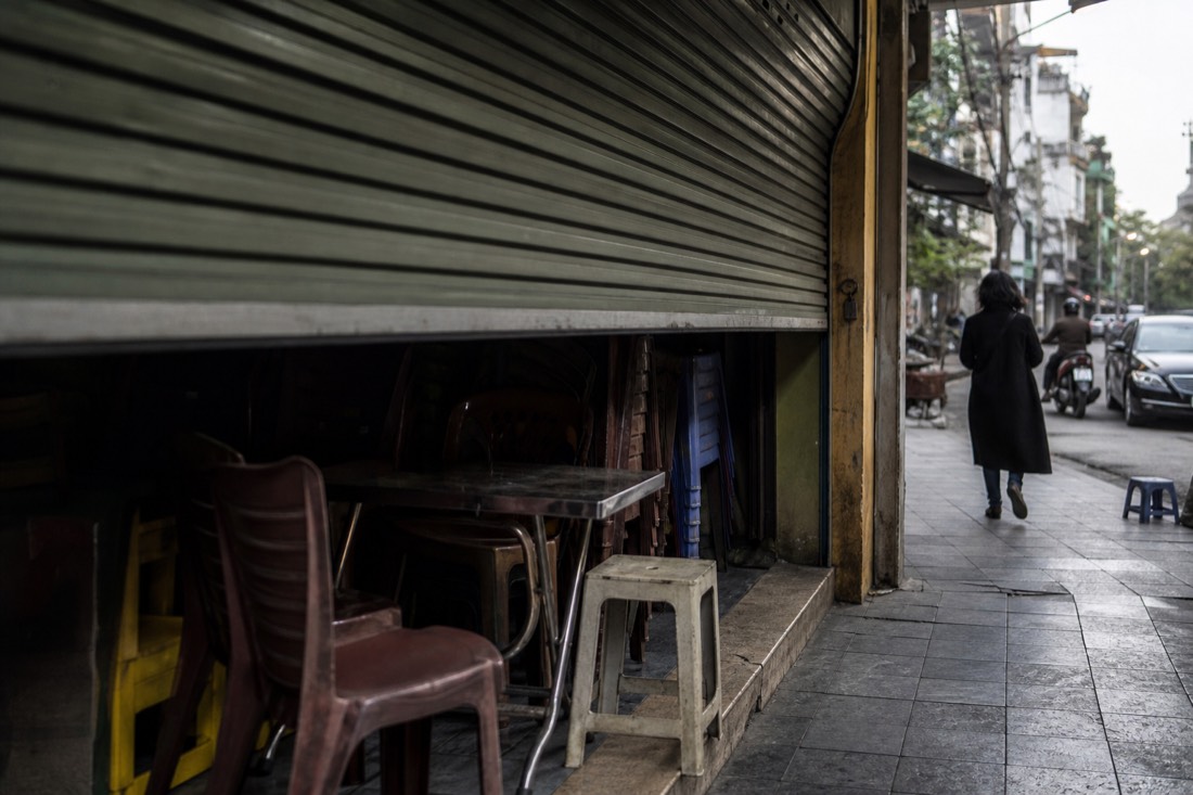 Shuttered Hanoi food stall with stacked chairs in the quiet gap between lunch and evening service