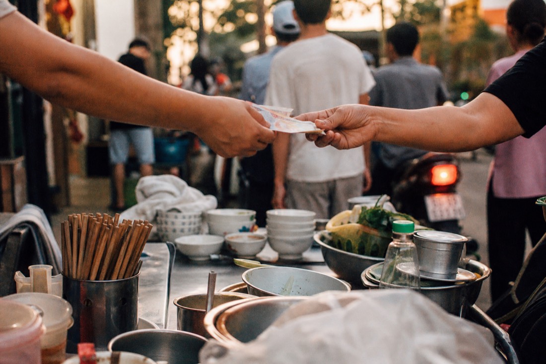 Hands passing small Vietnamese dong notes across a low street food counter in Hanoi