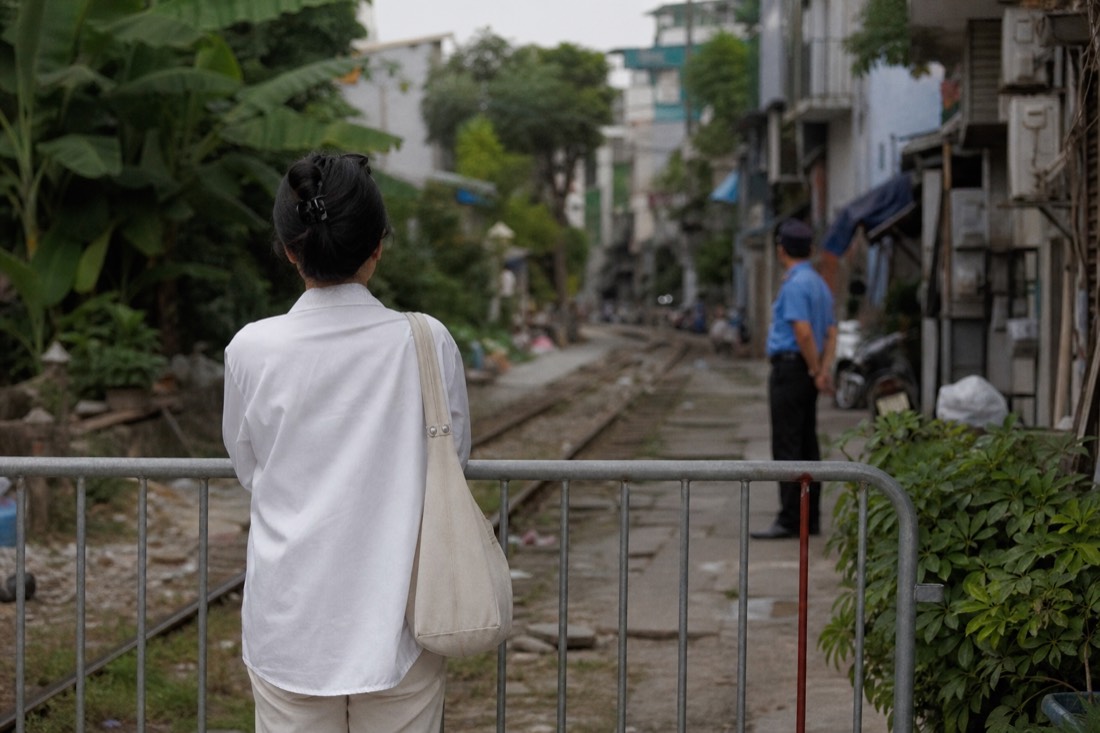 Visitor pausing at a manned barrier entrance to Hanoi's Train Street corridor