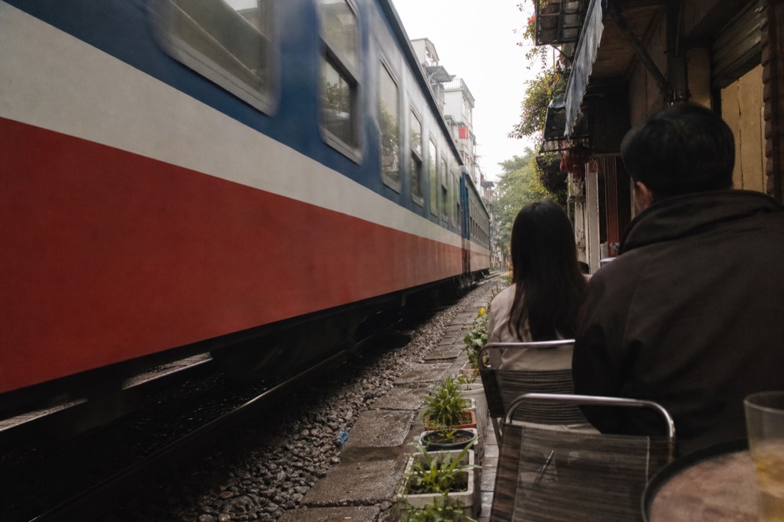 Train passing at arm's length beside cafe tables in Hanoi's Train Street corridor
