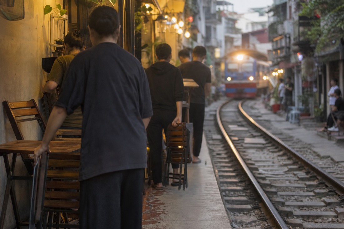Cafe staff folding stools beside the tracks in the Hanoi Train Street corridor before a train passes