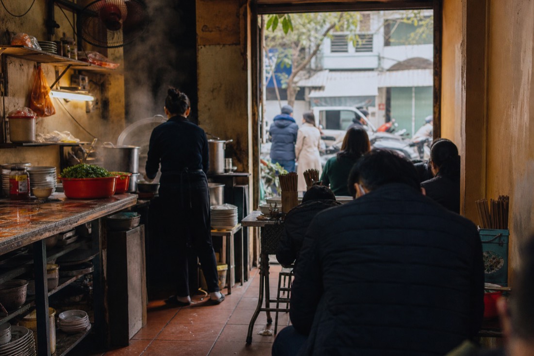 Old family-run Hanoi noodle shop interior with steaming pots and worn wooden stools