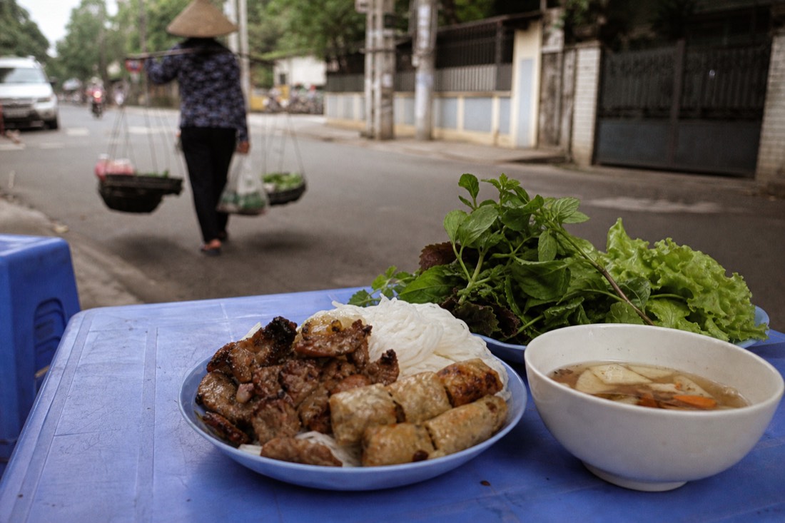 Plate of grilled pork bun cha with dipping sauce on a plastic table at a street-level shop