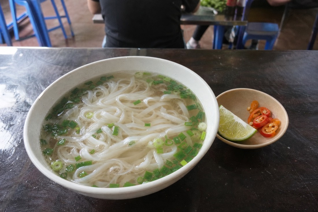 Bowl of clear northern-style pho with spring onion and a wedge of lime, no herb plate