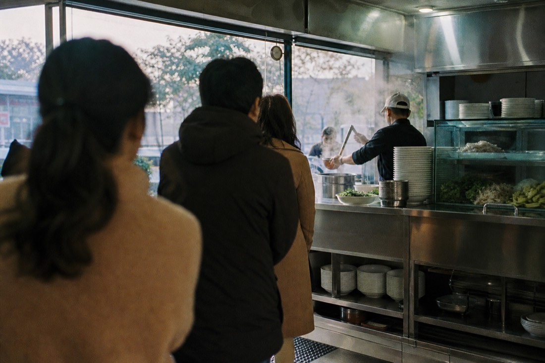 Queue of customers waiting at a self-service pho counter in Hanoi in early morning light