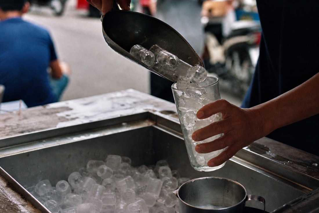 Hand scooping cylindrical factory ice into a glass at a Hanoi drink stall