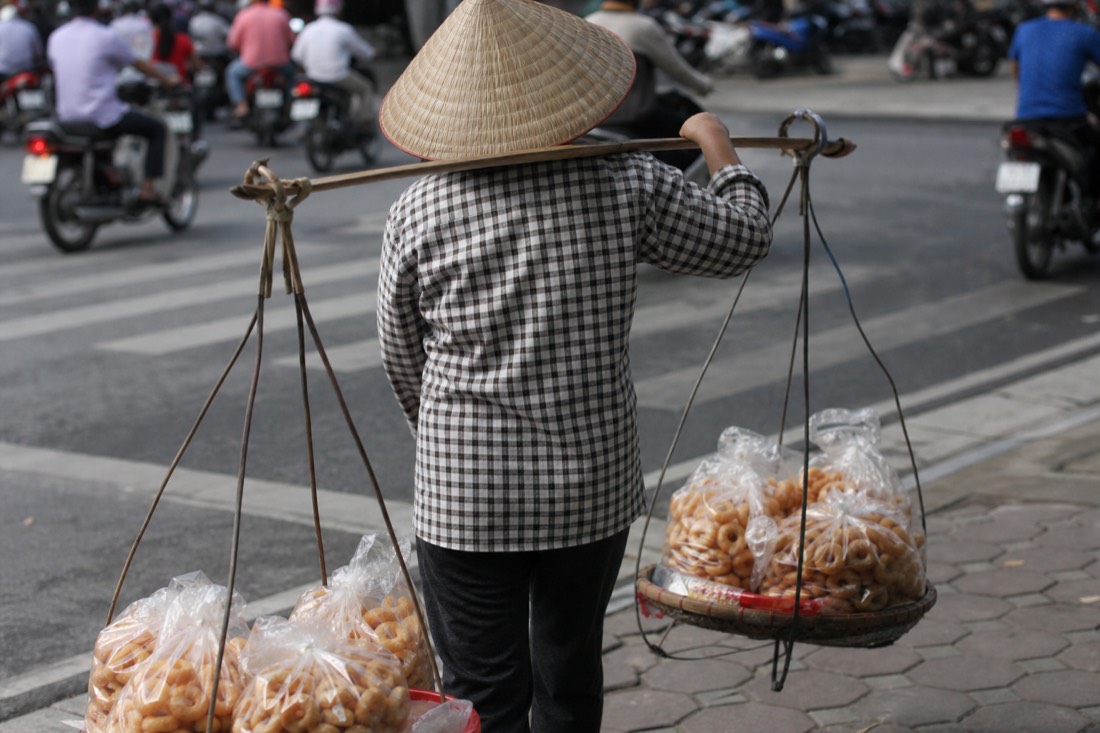 Bamboo shoulder pole with small bags of donuts balanced on a Hanoi street corner