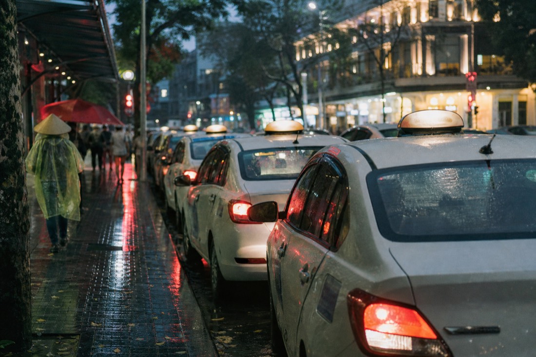 Row of taxis waiting curbside in Hanoi's Old Quarter at dusk with wet reflective pavement