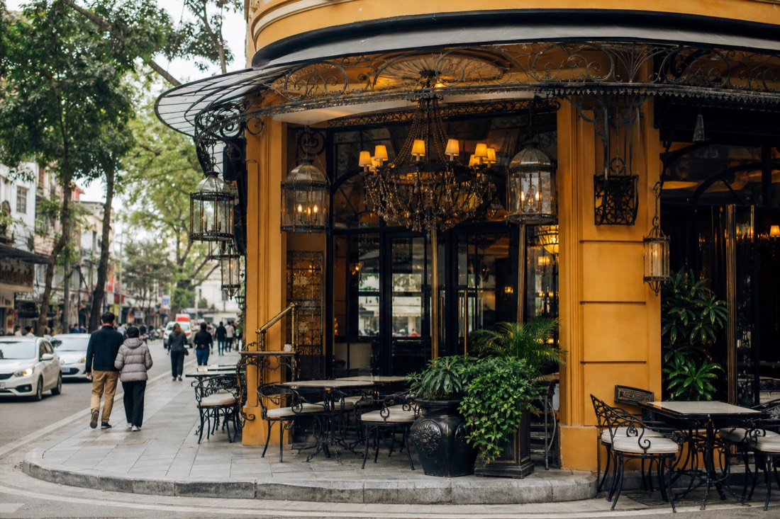 Ornate restaurant storefront on a premium corner near Hoan Kiem Lake with empty tables at midday