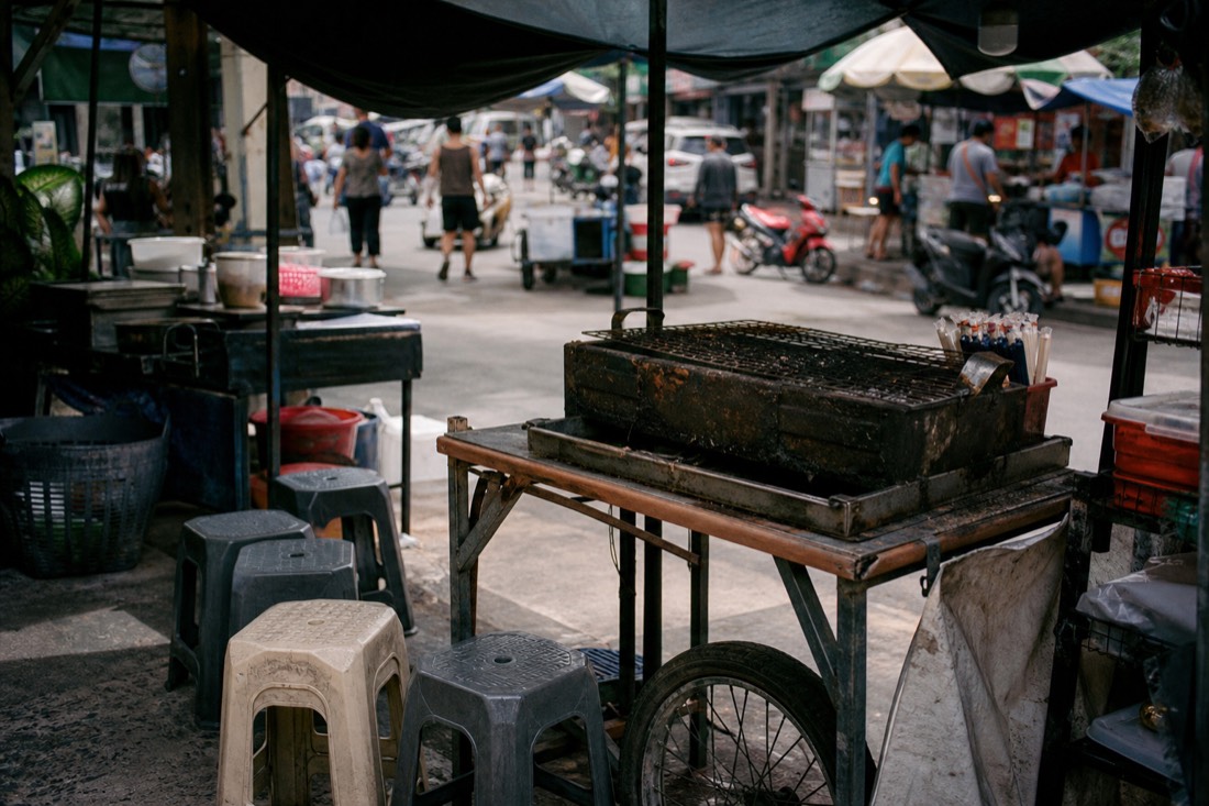 Unlit charcoal grill and empty stools at a quiet street food stall at midday in Hanoi