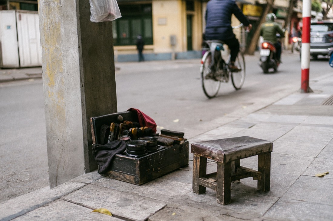 Shoe-shine kit and brushes laid on the pavement beside a stool at a Hanoi street corner
