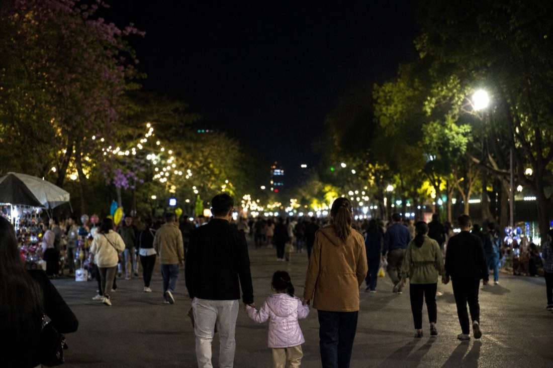 Pedestrianized street around Hoan Kiem Lake on a weekend evening filled with strolling families