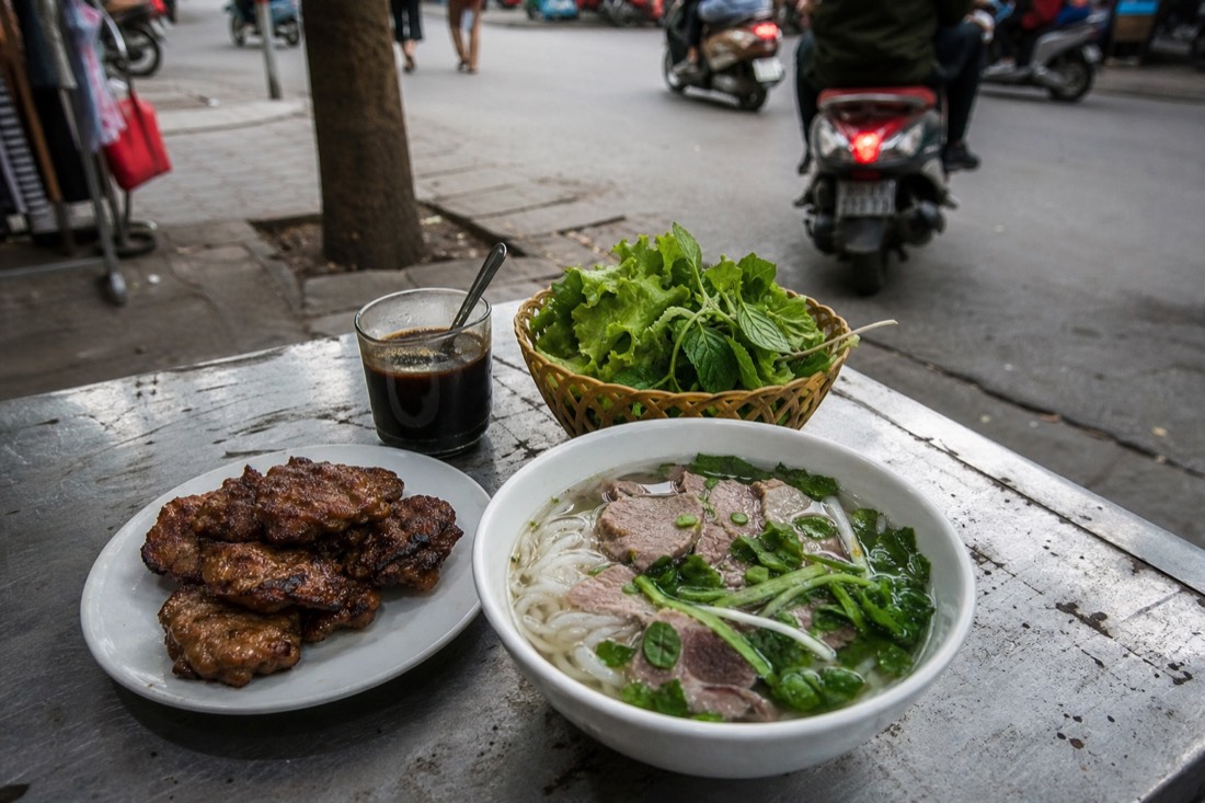 Assorted Hanoi dishes including pho, bun cha and egg coffee laid out on a street table