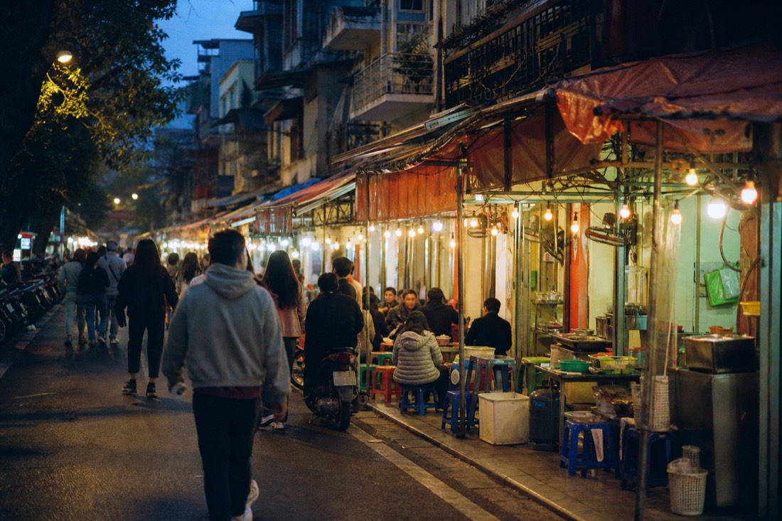 Evening food stalls glowing along a narrow Hanoi Old Quarter street on a guided walking tour
